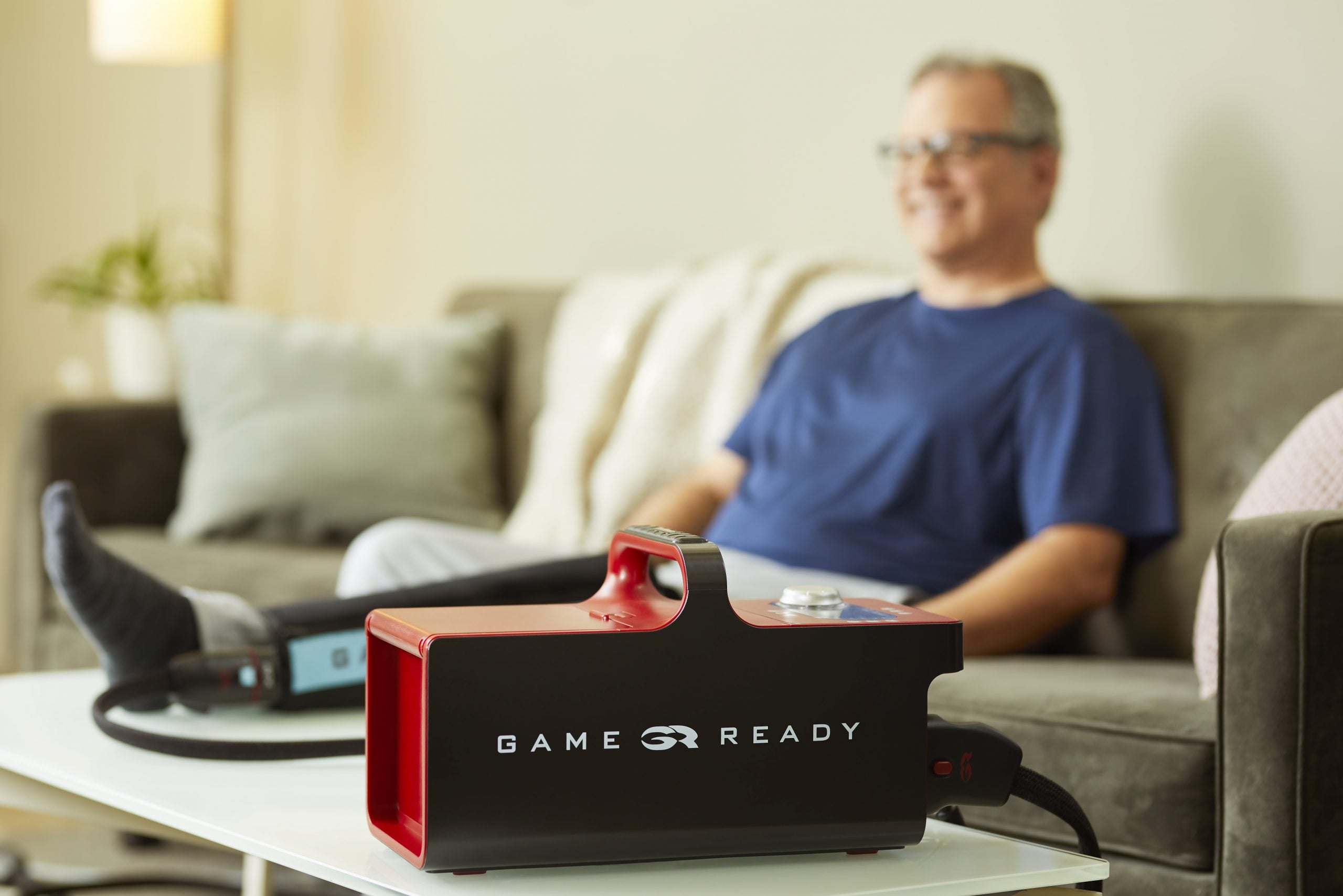 Uomo che utilizza il dispositivo Game Ready a casa, con fasciatura applicata alla gamba, seduto comodamente sul divano